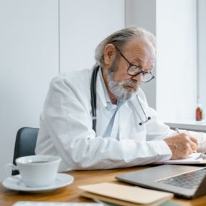 Elderly doctor sitting at desk writing note