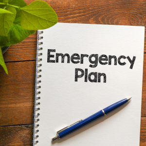 Notebook on desk with pen laying across it with the words Emergency Plan written on page