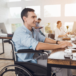 Smiling man in wheelchair sitting at desk looking at laptop