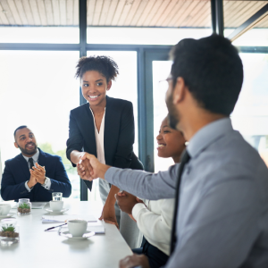 Four people sitting at board room table.  Woman shaking man's hand