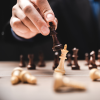 Man's hand with chess piece knocking over another chess piece on chess board