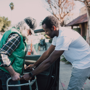 Young man helping elderly man out of car with his walker